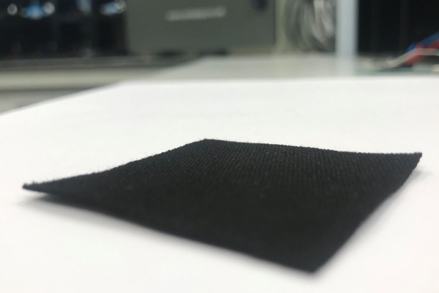 Close-up of a black square fabric swatch on a white surface.